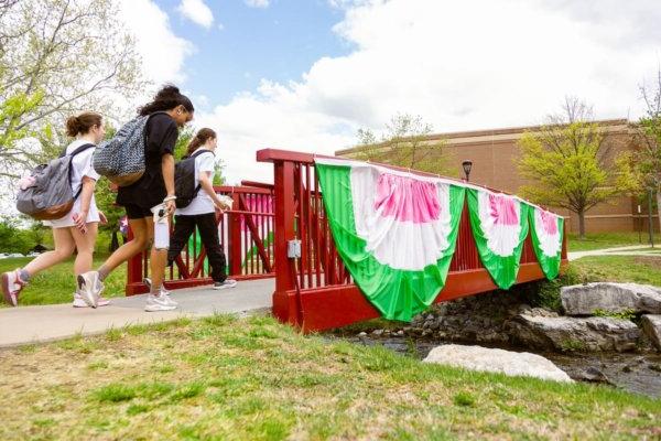 Shenandoah students walk across a bridge decorated with pink, white and green bunting.